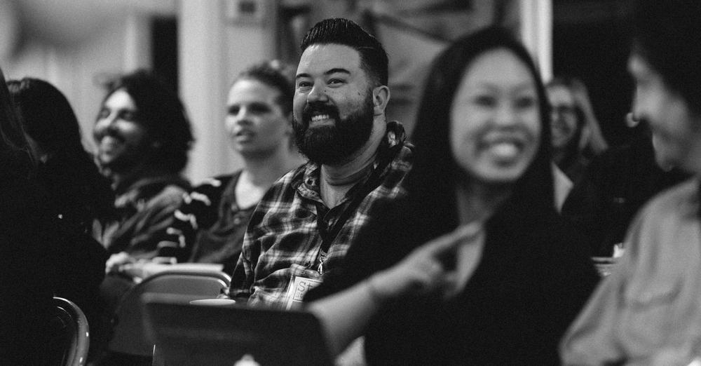 A black and white photo of men and women sitting in rows and smiling
